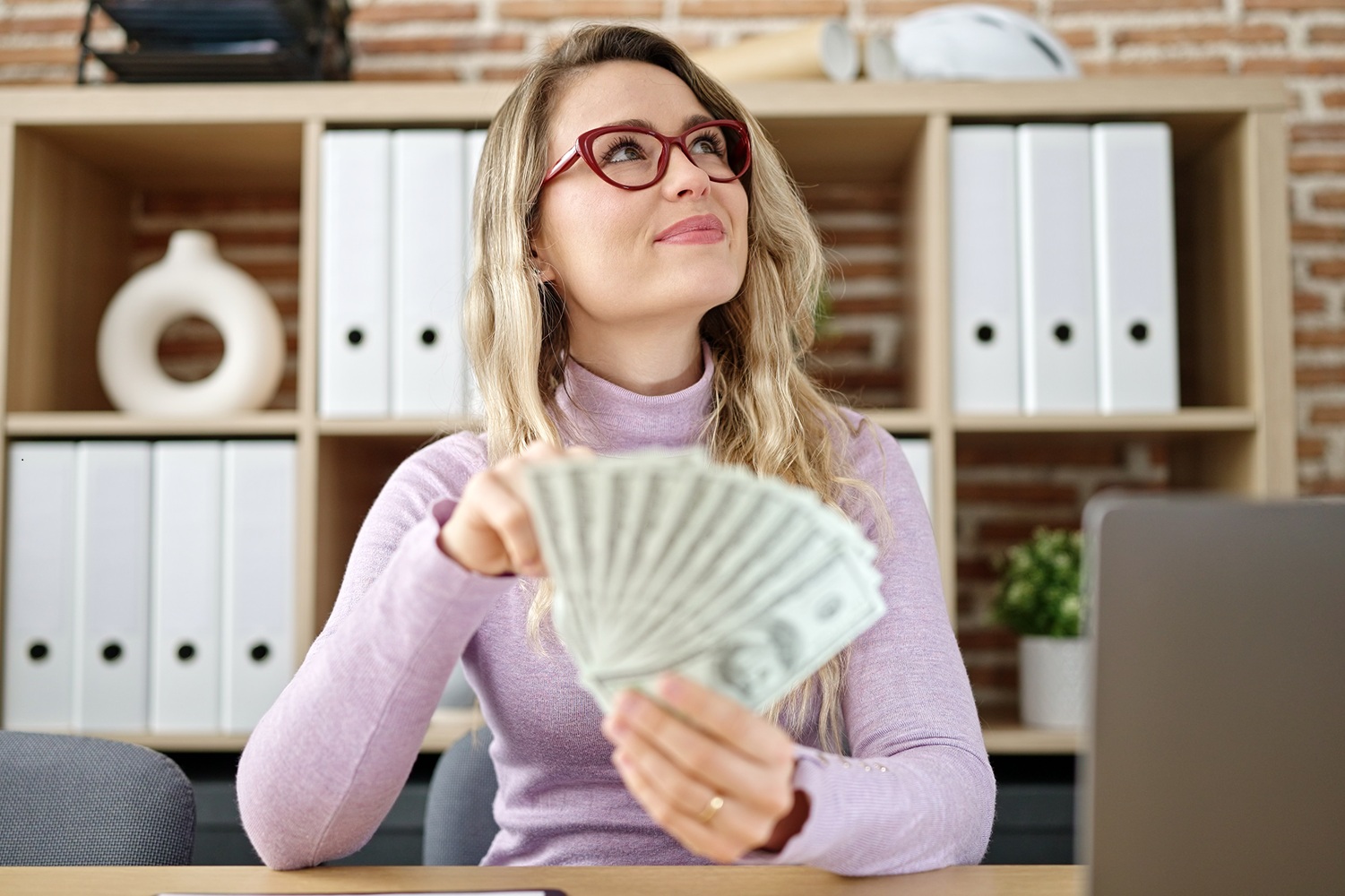 woman holding cash in front of laptop
